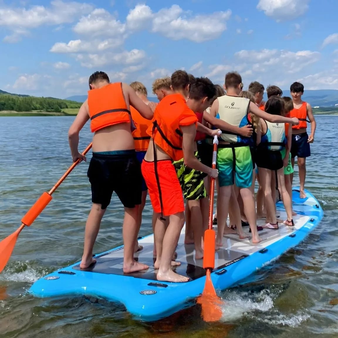 Skupina dětí na mega paddleboardu na jezeře Milada