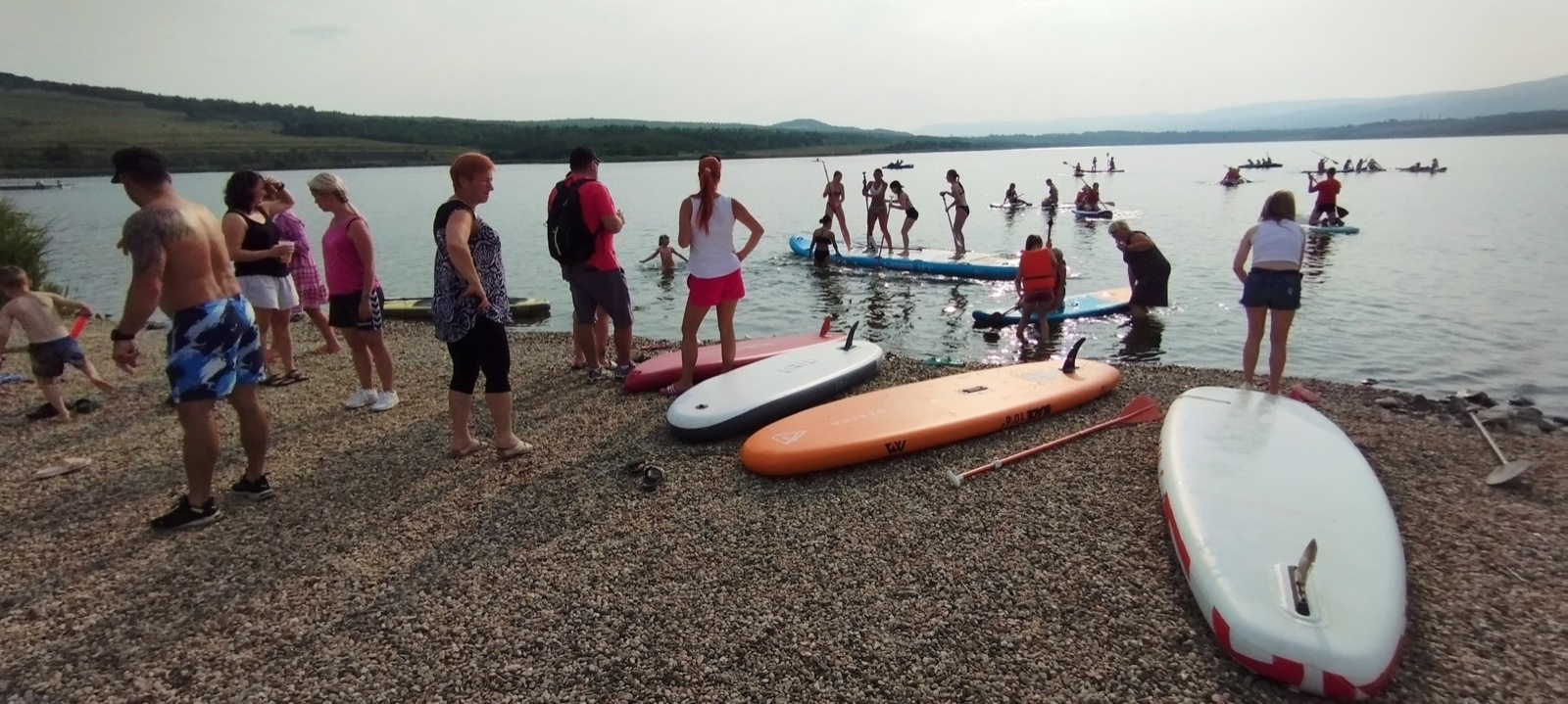 Lidé u vody s paddleboardy na jezeře Milada