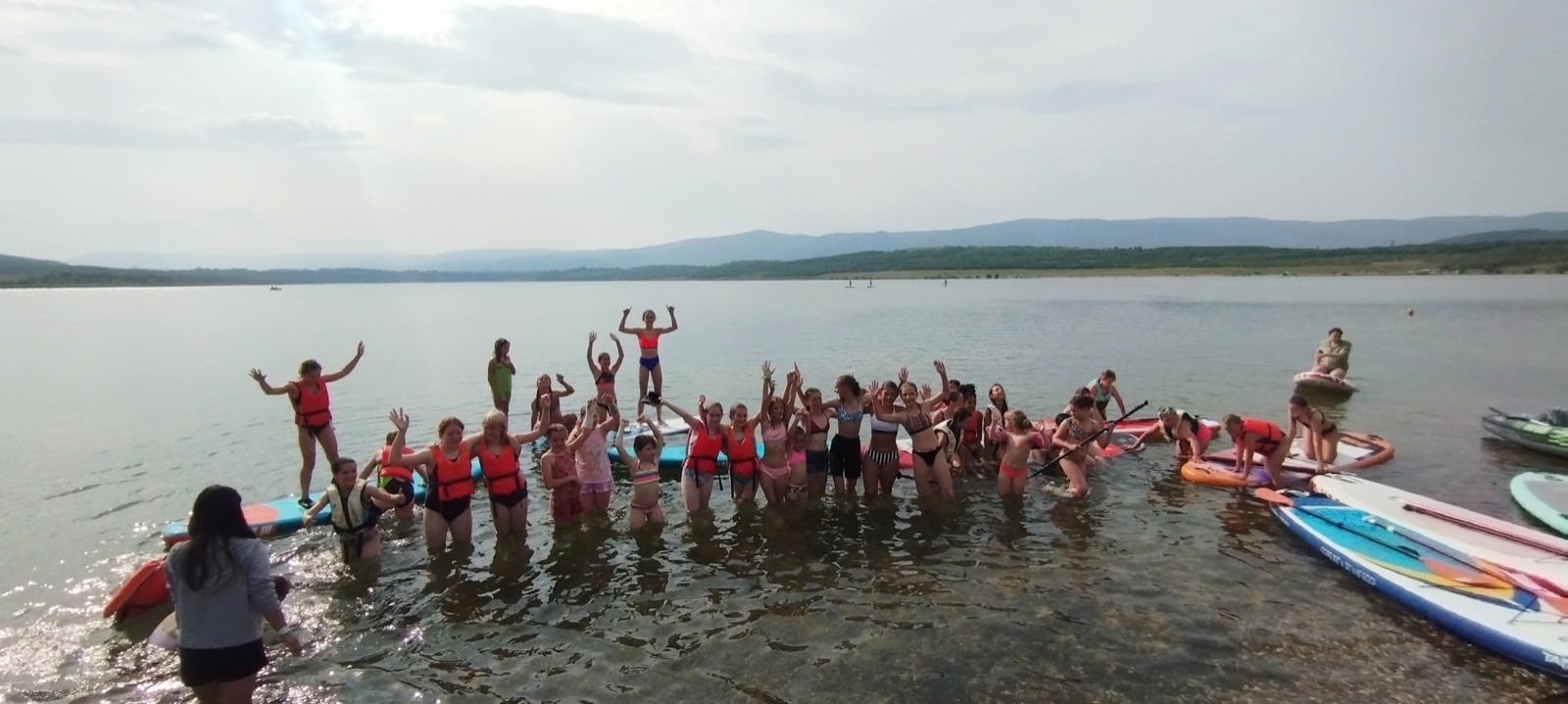 Skupina dětí se směje ve vodě s paddleboardy na jezeře Milada